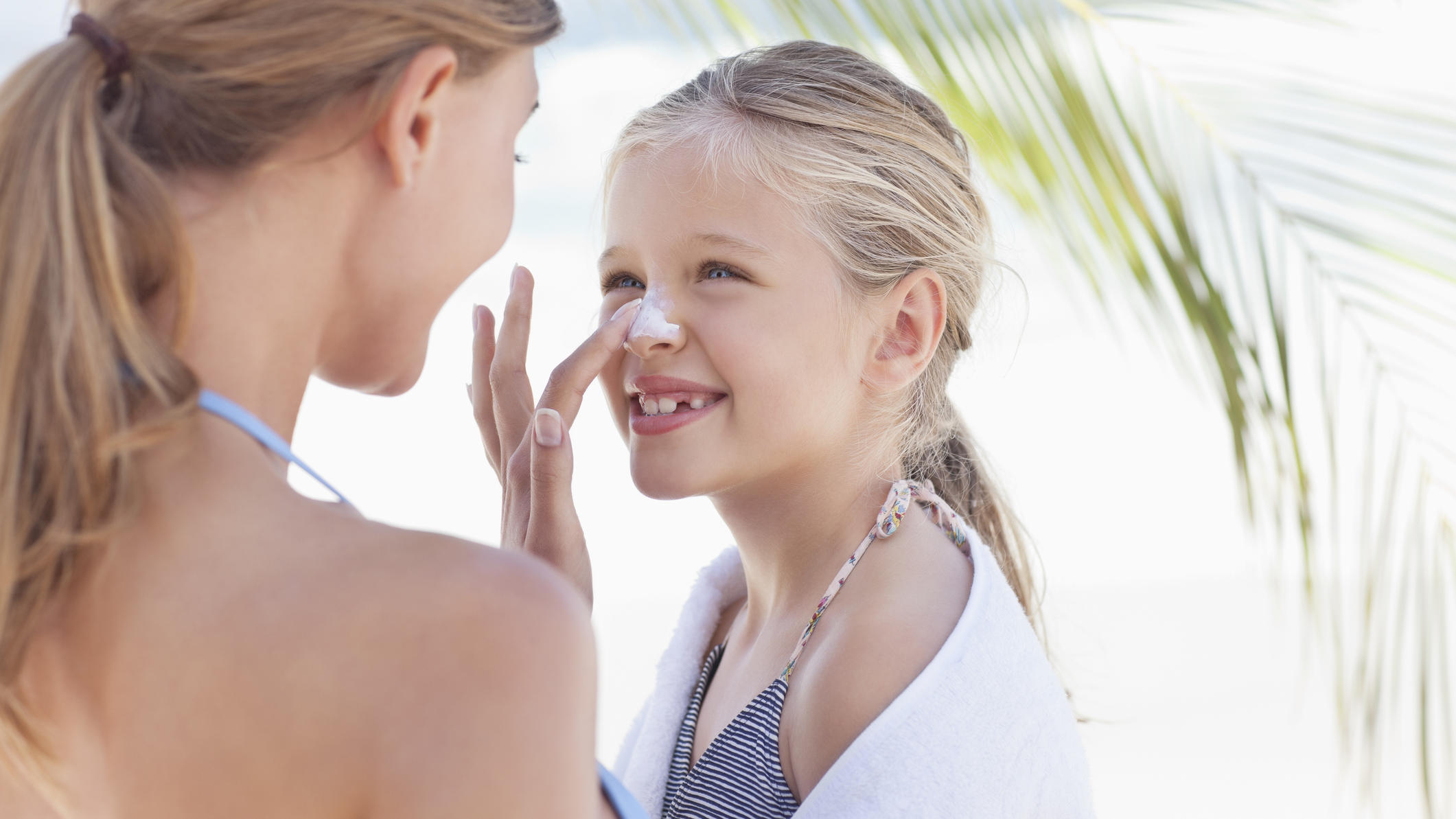 UV-Schutzkleidung für Kinder – darauf sollten Eltern achten Mutter cremt ihre Tochter ein.