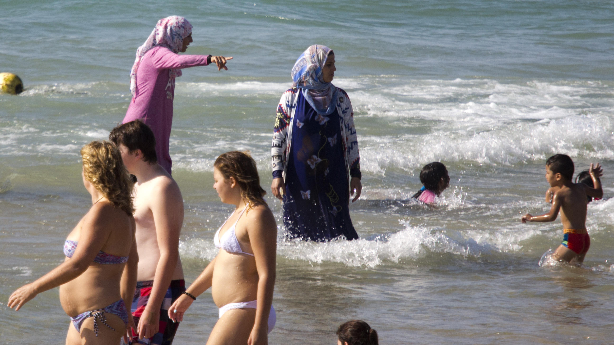 "Adam sucht Eva"-Frage: Warum schämen wir uns eigentlich nackt? Eine Frau im Burkini badet neben Menschen in Bikini und Badehose.
