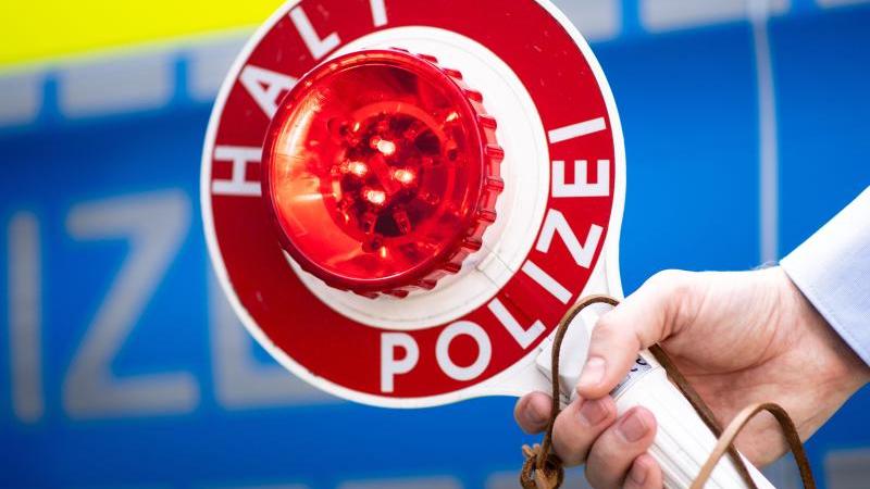 Mit zwei Handys am Steuer: Autofahrer in Polizeikontrolle Polizist hält eine Polizeikelle mit der Aufschrift «Halt Polizei»