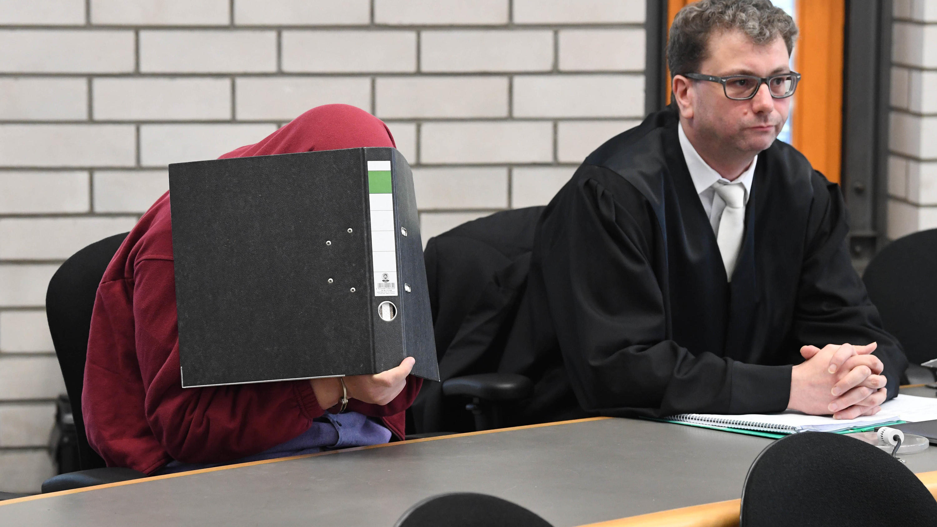 Urteil gegen Schwimmlehrer in Baden-Baden: 200 einzelne Taten in zwei Jahren ARCHIV - 19.09.2018, Baden-Württemberg, Baden-Baden: Ein 34 Jahre alter angeklagter Schwimmlehrer (l), dem vorgeworfen wird sich an kleinen Mädchen vergangen zu haben, wartet im Landgericht Baden-Baden mit einem Aktenordner vor dem Gesicht zusammen m