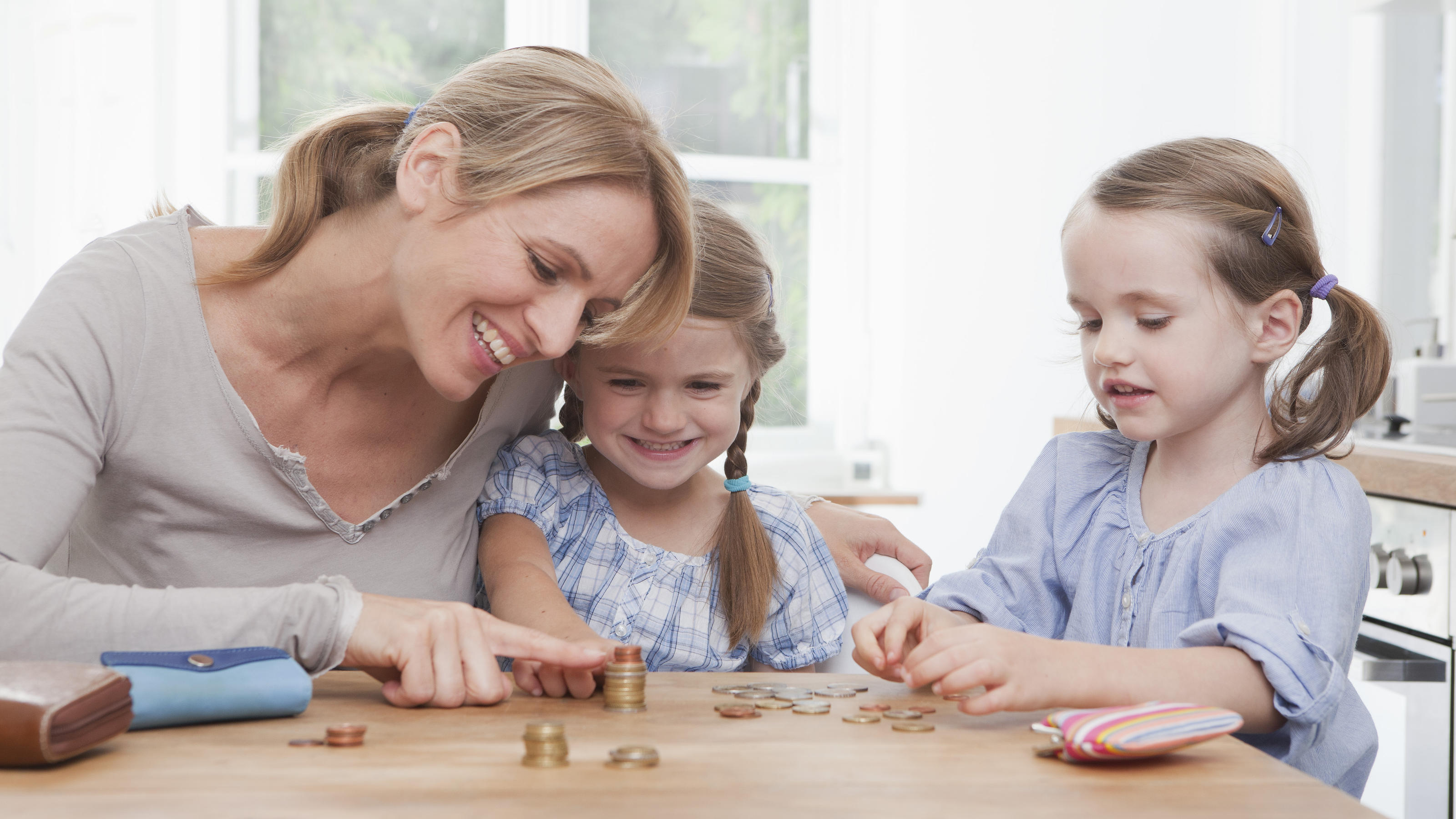 Kindergelderhöhung und weniger Steuern: Das ändert sich 2019 für Familien Mutter stapelt mit ihren Töchtern Geldstücke aufeinander.