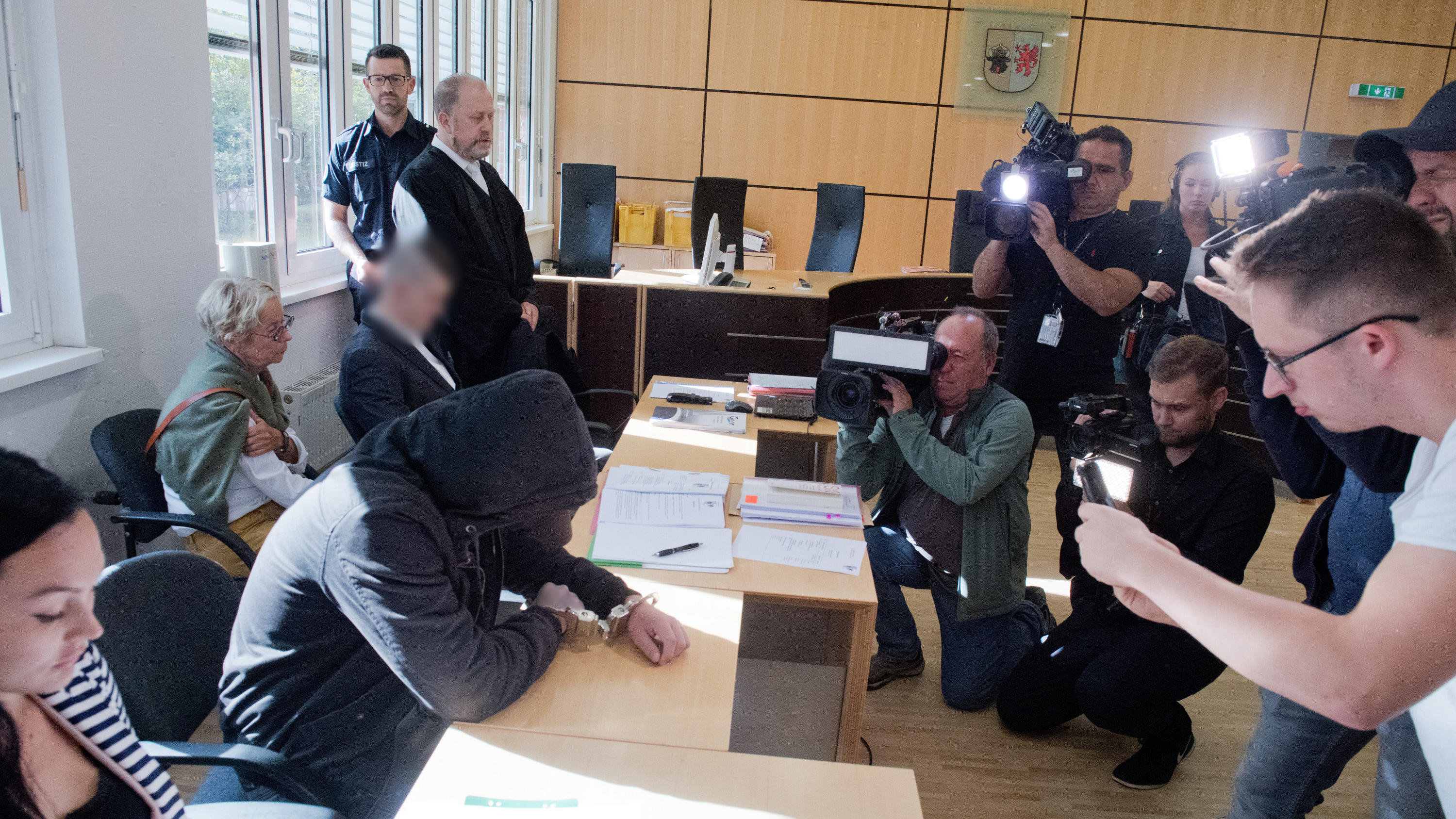 Angeklagter Nicolas K. legt Geständnis ab: "Klar, dass das Baby auch stirbt" 20.08.2019, Mecklenburg-Vorpommern, Stralsund: Der 19-jähriger Angeklagte (2.v.l.) verbirgt im Gerichtssaal im Landgericht sein Gesicht. Für den Mord an der 18-jährigen Maria aus Zinnowitz auf Usedom müssen sich am selben Tag der 19- und ein 21-Jähri