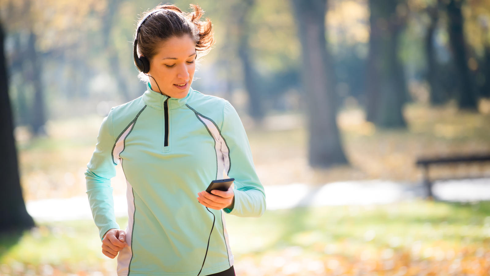 Sicher Joggen: Mit diesen Tipps verteidigen Sie sich im Ernstfall! Young woman with headphones jogging in autumn nature and looking to mobile phone