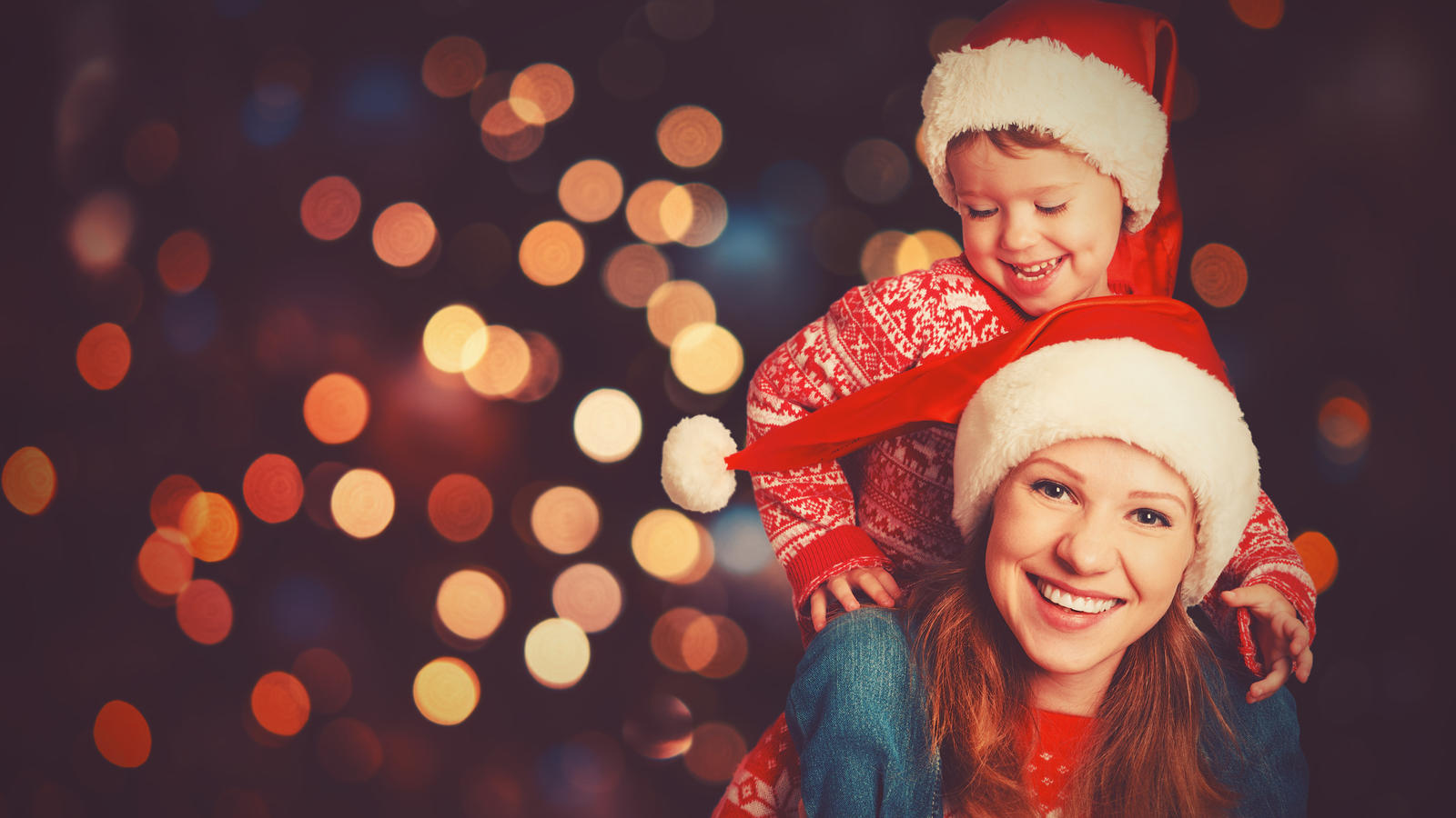 Kindern vom Weihnachtsmann erzählen: Wann ist der richtige Zeitpunkt für die Wahrheit? Mutter und Sohn mit Weihnachtsmützen stehen glücklich vor ihrem Weihnachtsbaum