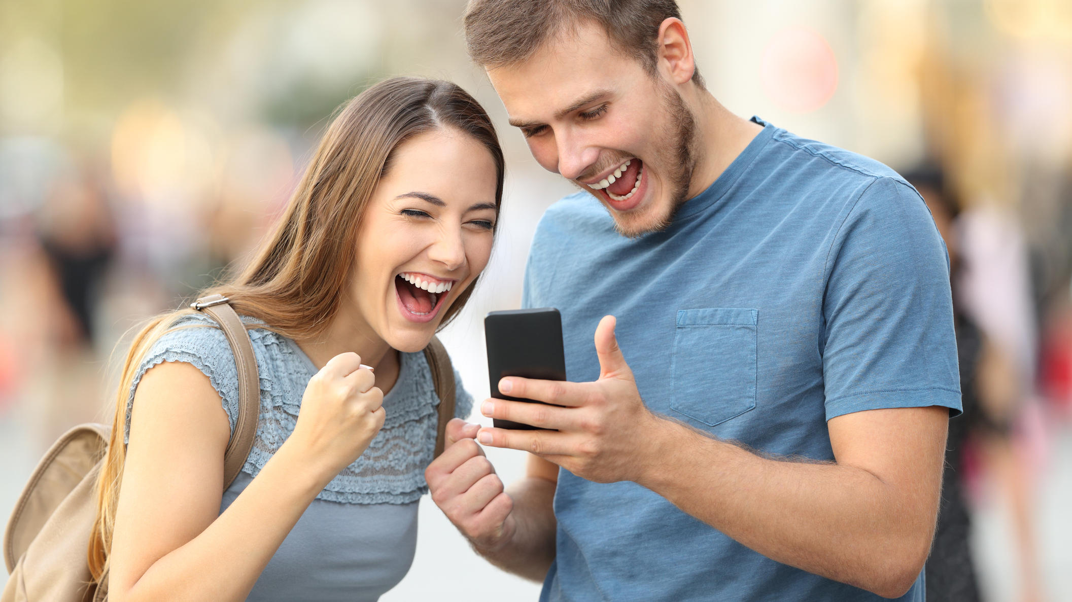 WhatsApp-Nachrichten länger als nach sieben Minuten löschen? Bald soll das möglich sein Excited couple receiving good news on line in a smart phone outside on the street
