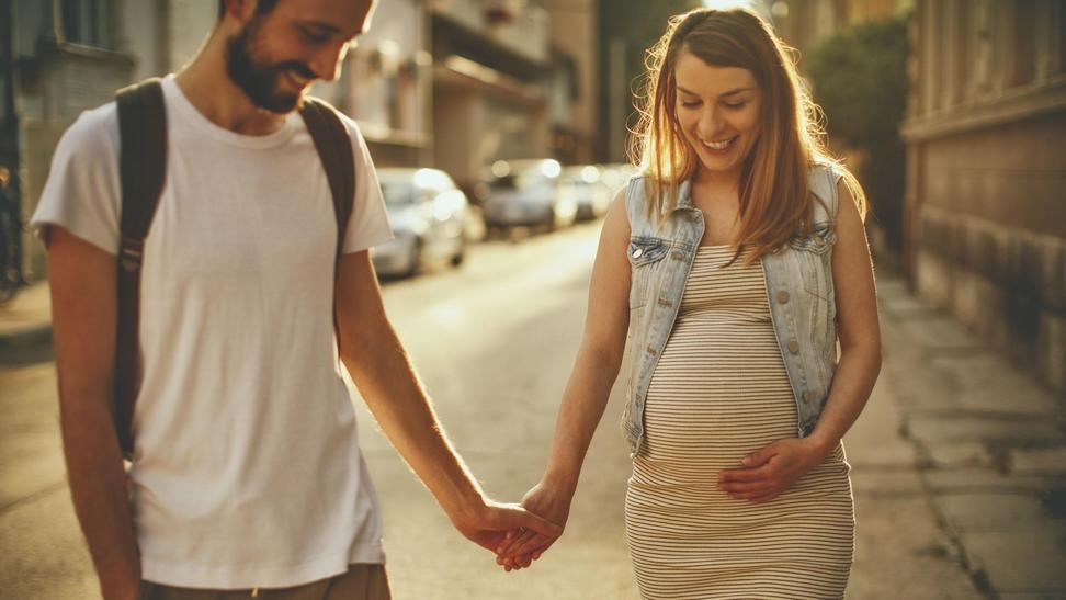 Schwangere Frau geht Hand in Hand mit ihrem Partner eine Straße entlang. 