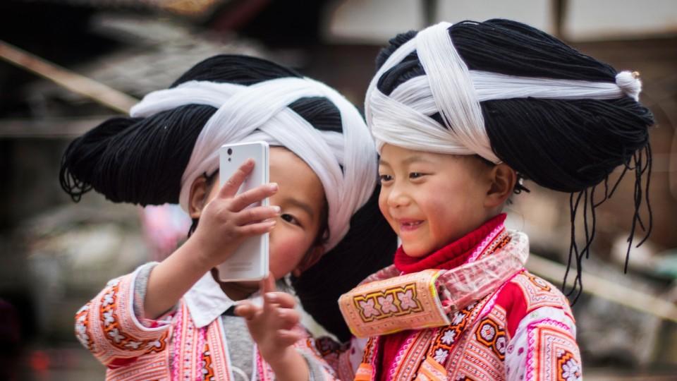Mädchen des Long Horn Miao-Volks in China posieren für ein Selfie mit ihren großen Perücken, das von den Haaren ihrer Vorfahren gemacht wurde.